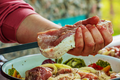 A bowl filled with marinated raw meat and women's hands stringing kebabs on a skewer