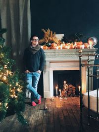 Full length of young man standing by illuminated christmas tree at home