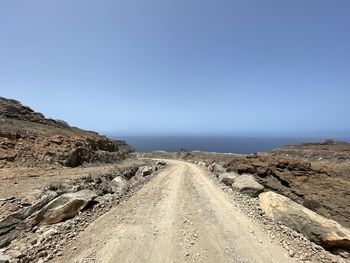 Dirt road amidst land against clear sky