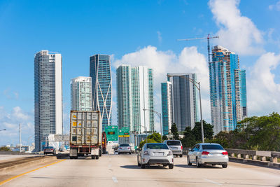 Cars on road by buildings against sky in city