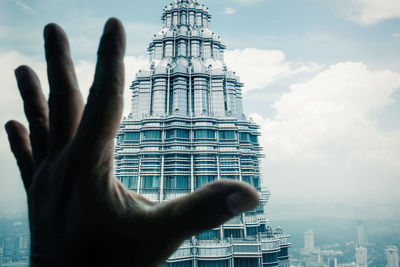 Cropped hand of person against buildings and sky