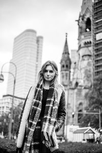 Portrait of young woman standing against buildings in city