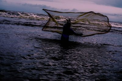 Rear view of man fishing in sea against sky