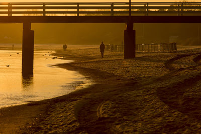 Silhouette men by bridge against sky during sunset