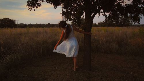 Woman standing by tree on field during sunset