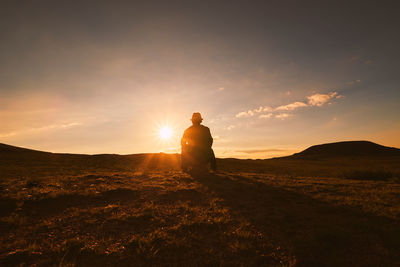 Silhouette man sitting on field against sky during sunrise