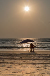 Silhouette men on beach against sky during sunset