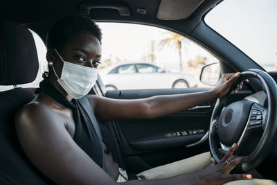 Woman with protective face mask driving car