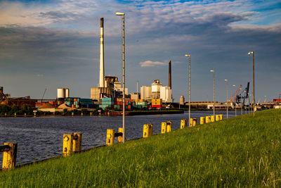 Factory by river against sky
