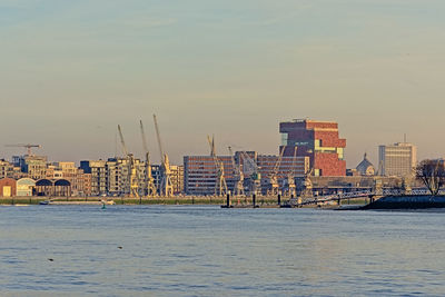 Sailboats in sea by buildings against sky