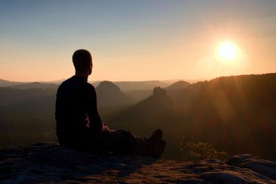 Silhouette man sitting on mountain against sky during sunset