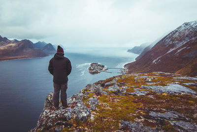 Rear view of man standing on cliff by sea against sky