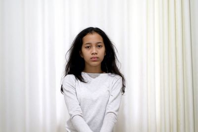 Portrait of teenage girl standing against curtain