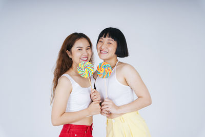 Lesbian couple holding lollipop against white background