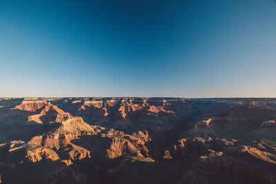 Scenic view of eroded landscape against clear blue sky during sunset