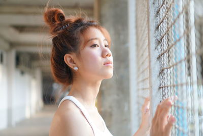 Young woman looking away while standing by window