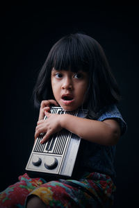 Portrait of cute girl holding radio against black background