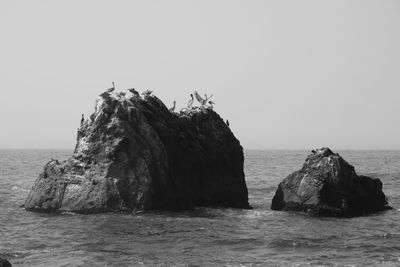 Rock formation in sea against clear sky