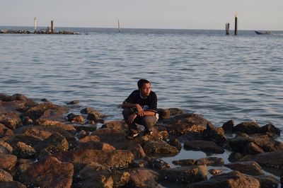 Man sitting on rock by sea against sky