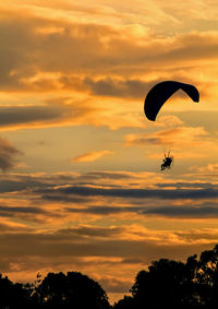 Low angle view of person powered paragliding in cloudy sky during sunset