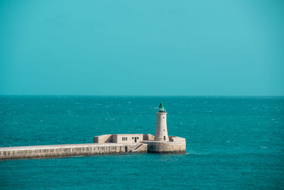 Lighthouse by sea against blue sky