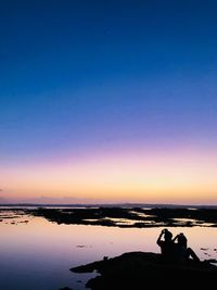 Silhouette people sitting on beach against sky during sunset