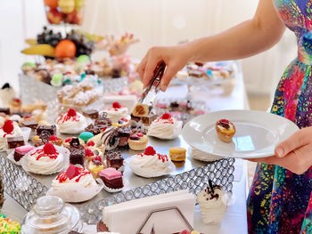 High angle view of woman picking up homemade colorful cakes on table