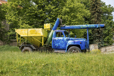 Old heavy truck machinery parked on grass against trees in historic town