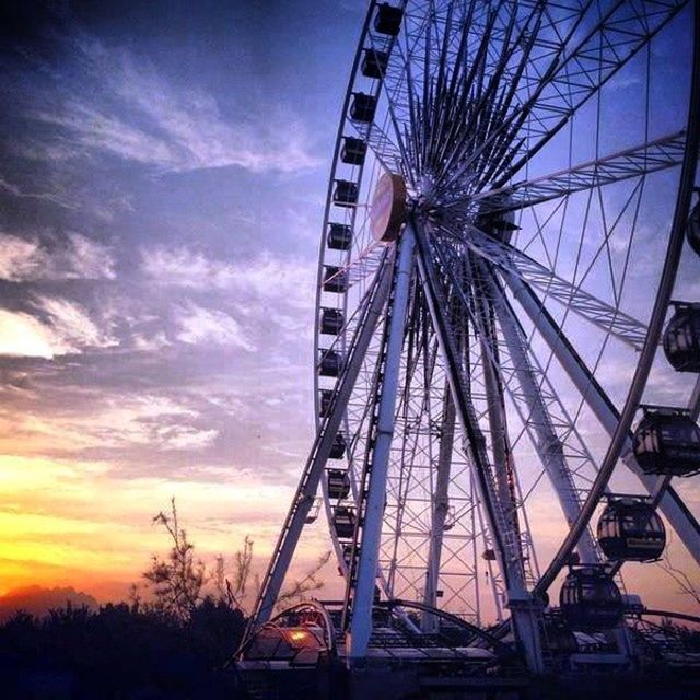 low angle view, ferris wheel, sky, amusement park, arts culture and entertainment, amusement park ride, cloud - sky, silhouette, built structure, sunset, tree, cloud, architecture, dusk, outdoors, metal, no people, large, cloudy, day