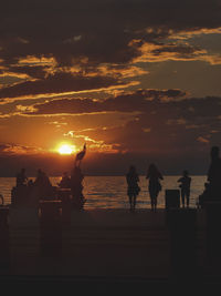 Silhouette people on beach against sky during sunset