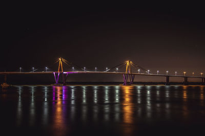 Illuminated bridge over sea against clear sky at night