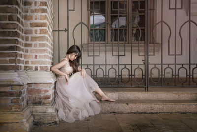 Full length of woman sitting against building