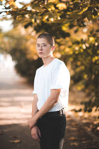 Stylish teen boy 14-16 year old wearing trendy clothes and glasses posing outdoors over green nature