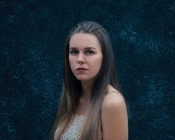 Portrait of young woman standing against blue background