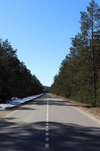 Empty road along trees and against blue sky