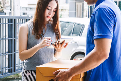 Woman signing on digital tablet while salesman holding cardboard box