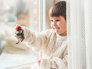 Kid with felt decorative snowman for christmas tree. boy in cable-knit oversized sweater. 