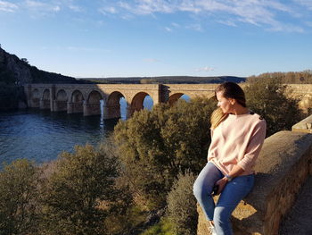Woman sitting on arch bridge against sky