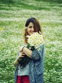 Happy woman holding white daisies while standing on field