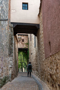 Rear view of woman walking on alley amidst buildings