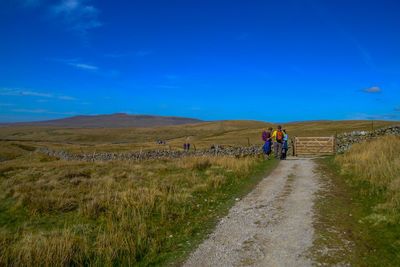 People on road amidst field against blue sky