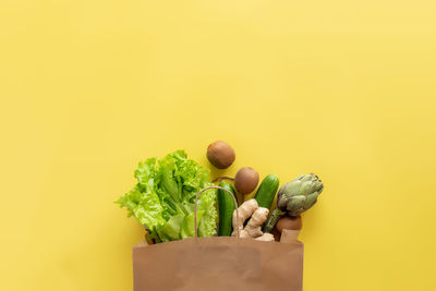 Yellow background. eco bag with lettuce salad leaves, kiwi, cucumber, artichoke and ginger root.