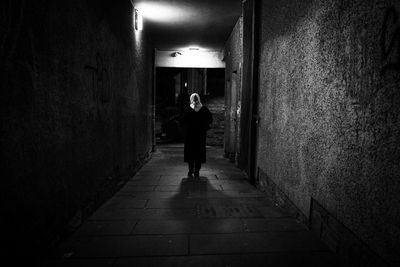 Rear view of man walking on footpath amidst illuminated building