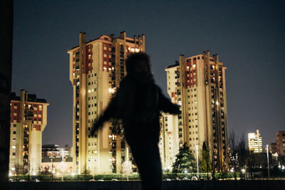 Man standing by illuminated buildings against sky at night