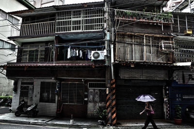 Woman walking with umbrella against building in city