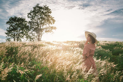 An asian girl on a beautiful spring meadow at sunset. she wears a pink dress and wide-brimmed hat.