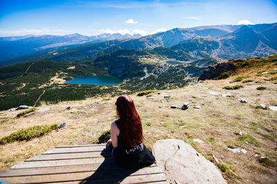 Rear view of woman sitting on mountain against sky