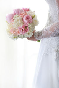 Midsection of bride holding bouquet while standing by curtain in wedding ceremony