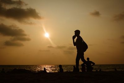 Silhouette people on beach against sky during sunset