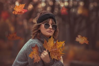 Portrait of woman wearing sunglasses amidst falling maple leaves during autumn
